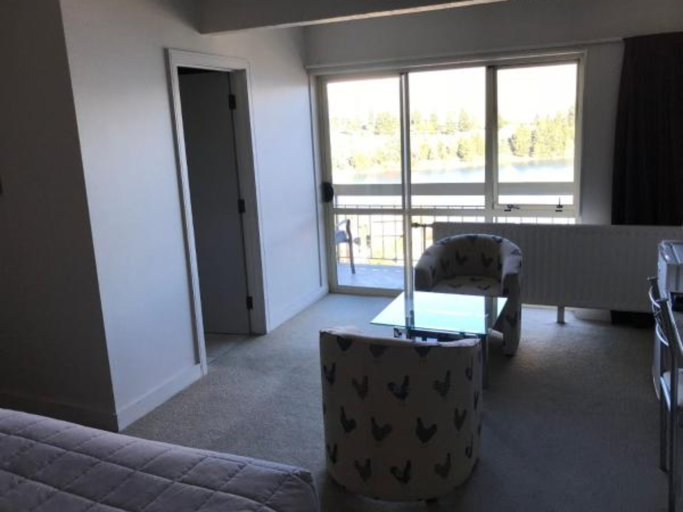 Una habitación con cama, una mesita, una silla y una ventana con vistas a árboles.