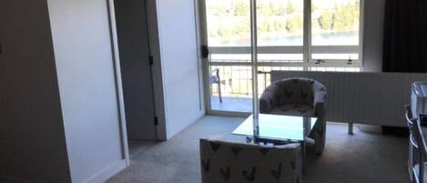 Una habitación con cama, una mesita, una silla y una ventana con vistas a árboles.