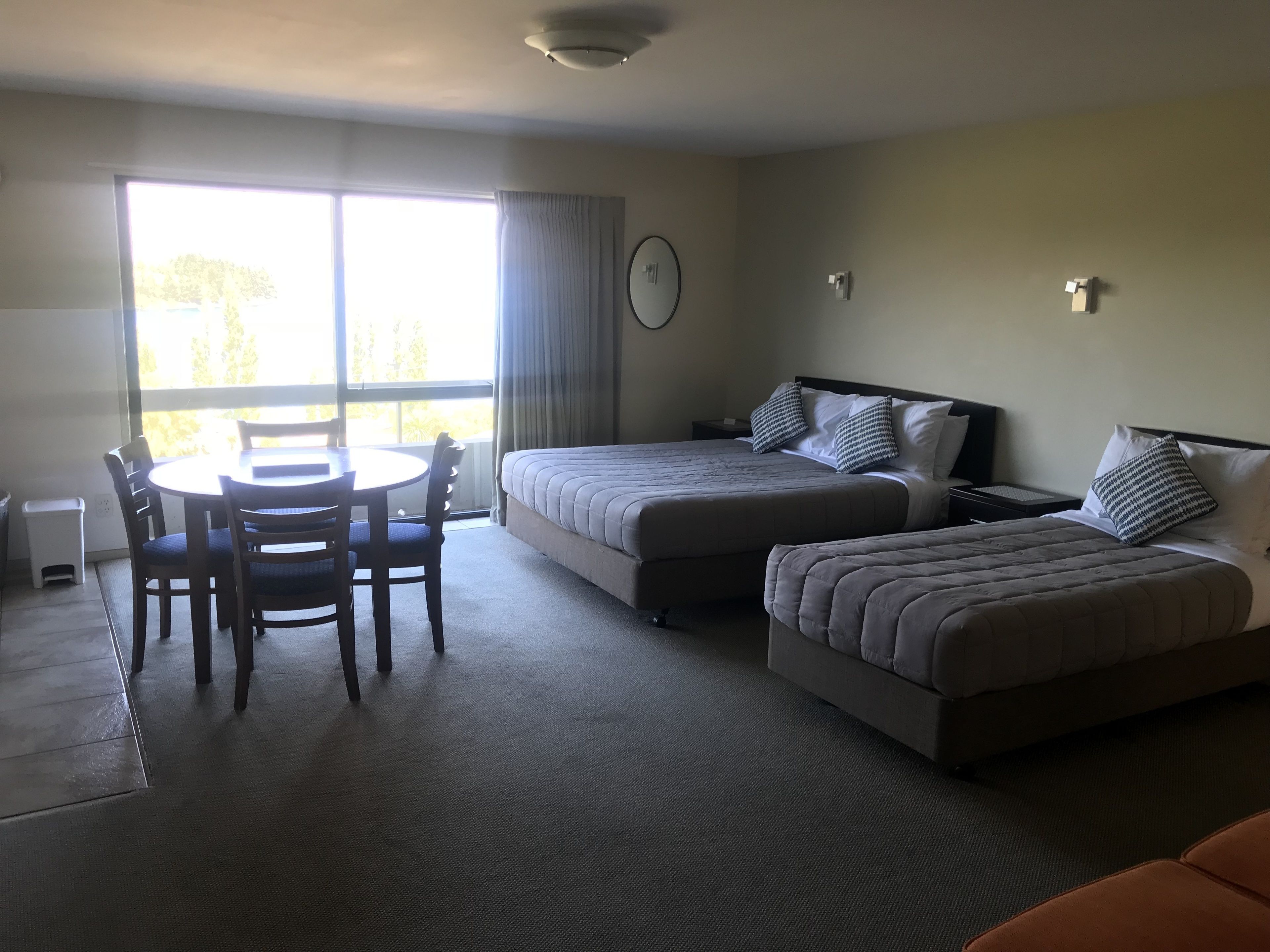 A hotel room with two beds, a dining table with chairs, and a view of the outdoors.