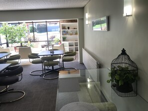 Una sala de reuniones moderna con mesas de vidrio, sillas tapizadas en verde, una estantería y una jaula con plantas.