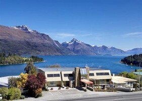 A hotel with a modern design, located near a lake with mountains in the background.