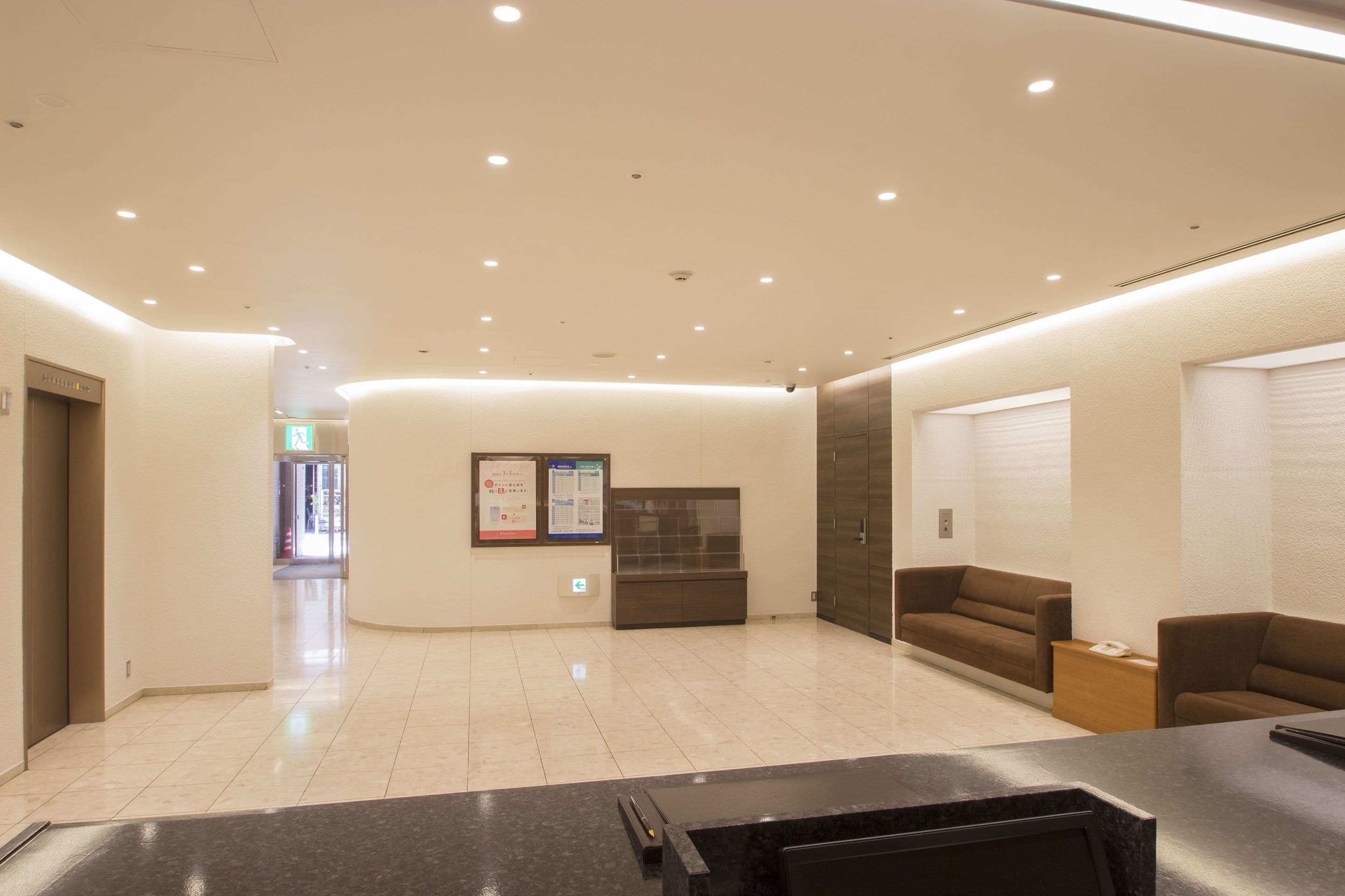 A modern hotel lobby with a reception desk, seating area, and a wall-mounted information board.