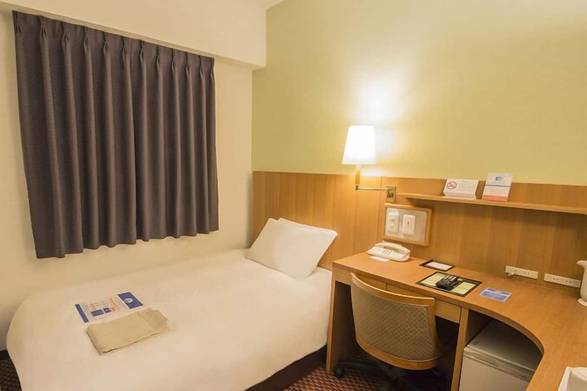 Habitación de hotel con cama, escritorio, silla, televisión, lámpara y repisa con objetos.