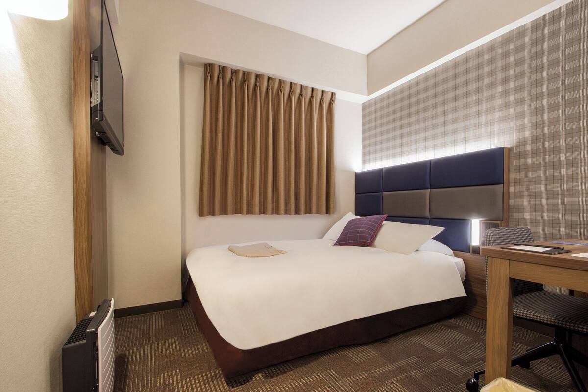 A hotel room with a large bed, a desk, and a television mounted on the wall.