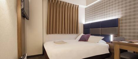 Una habitación de hotel con una cama grande, un escritorio y un televisor montado en la pared.