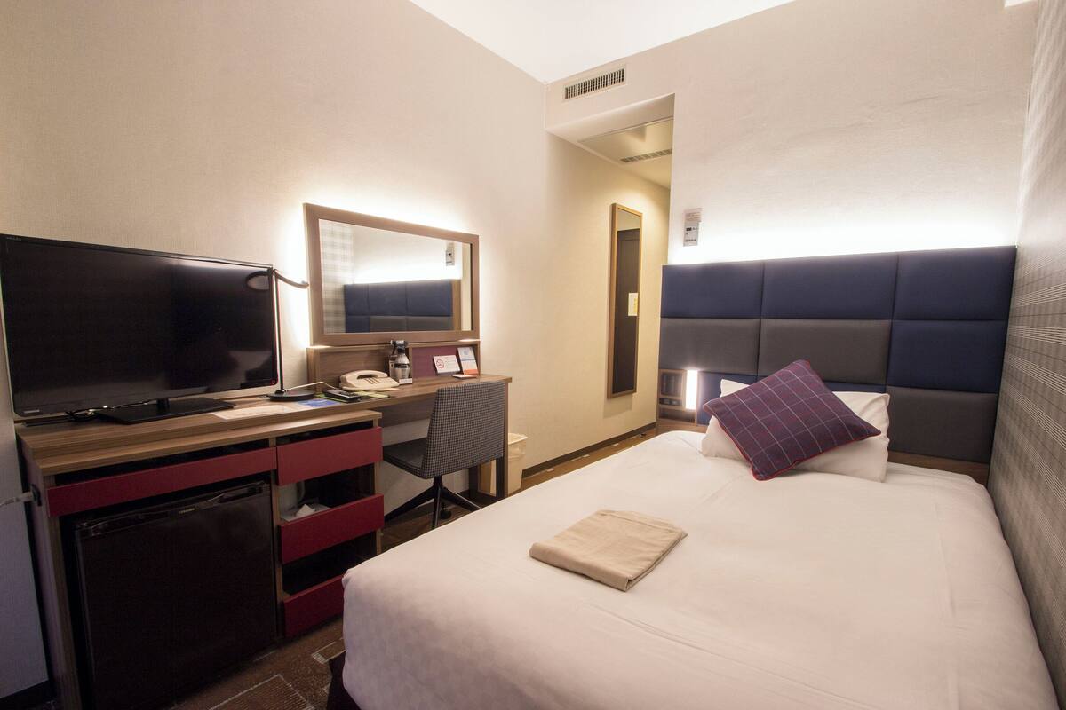A hotel room with a bed, a desk with a computer, a television, and a mirror.