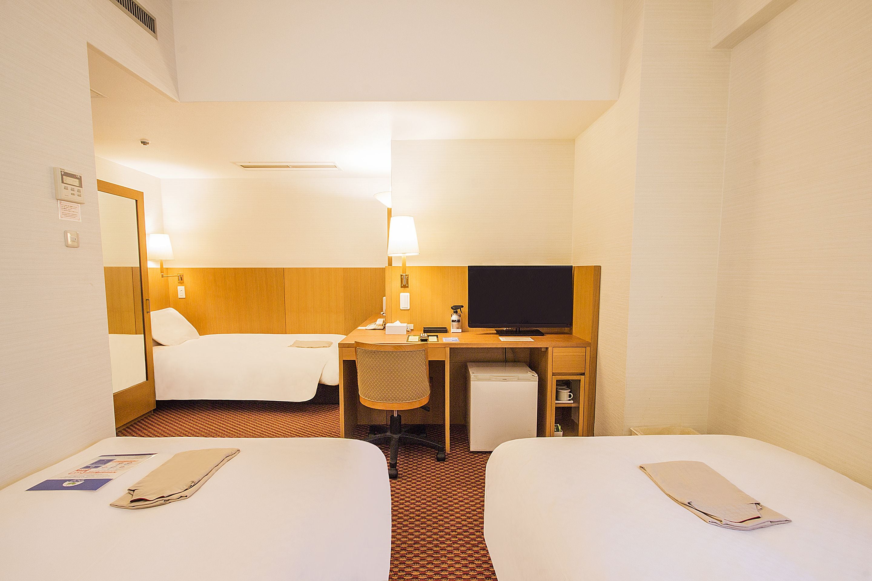 A hotel room with two beds, a desk with a computer, a TV, and a small refrigerator.