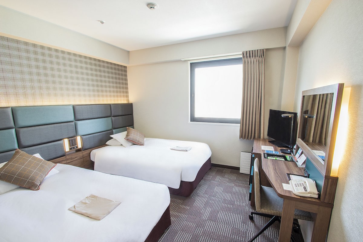 A hotel room with two beds, a desk, a computer, and a window with curtains.
