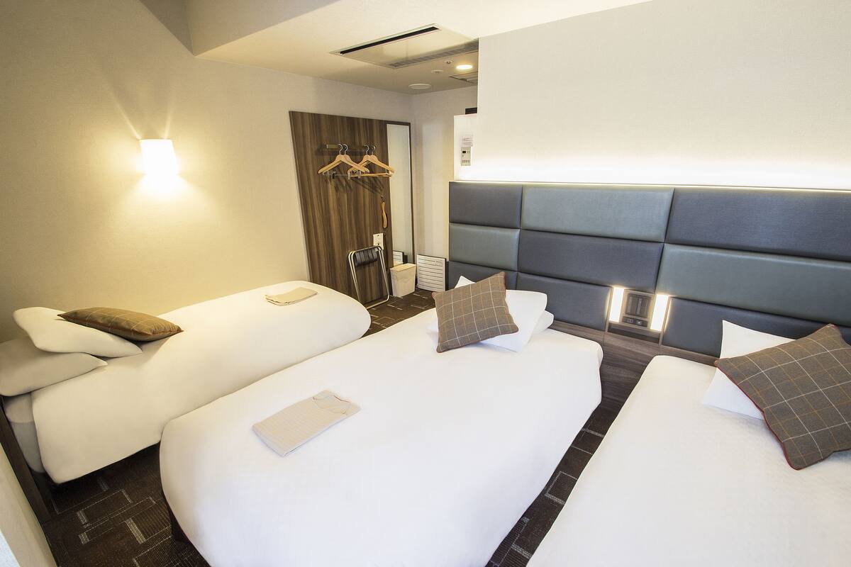 A hotel room with two beds, a seating area, a wooden door, and a wall-mounted light fixture.
