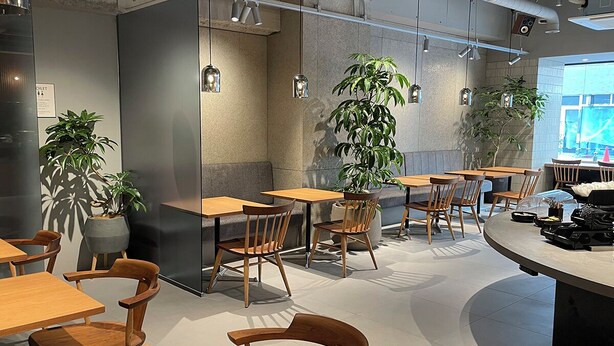 A modern cafe with wooden tables and chairs, potted plants, and a large window. - Hearton Hotel Shinsaibashi (Osaka)