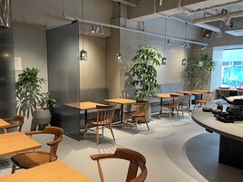 Un café moderne avec des tables et des chaises en bois, des plantes en pot et une grande fenêtre.