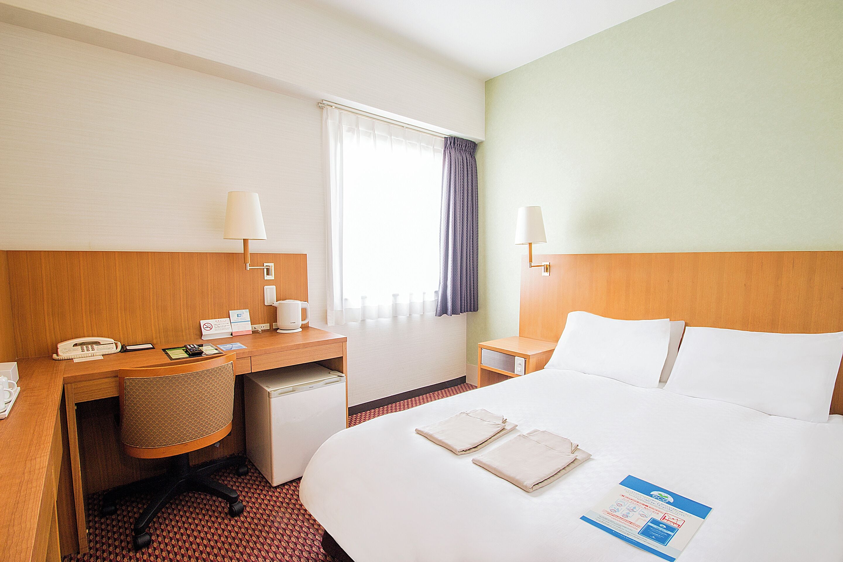 A hotel room with a bed, desk, chair, and a small kitchenette.
