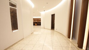 A corridor with a tiled floor, white walls, and a wooden door at the end. - Hearton Hotel Shinsaibashi (Osaka)