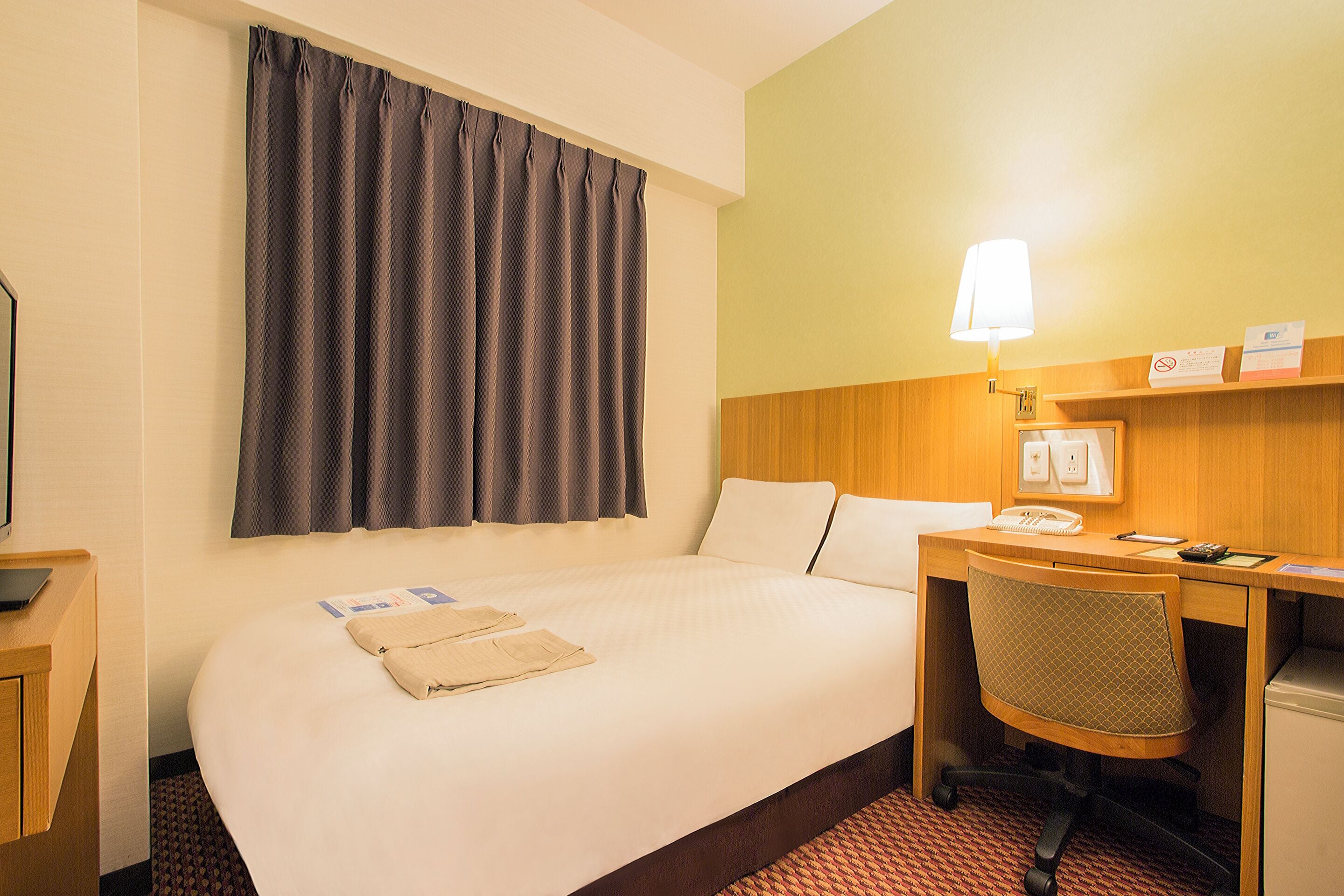 A hotel room with a large bed, a desk with a chair, a lamp, and a telephone.