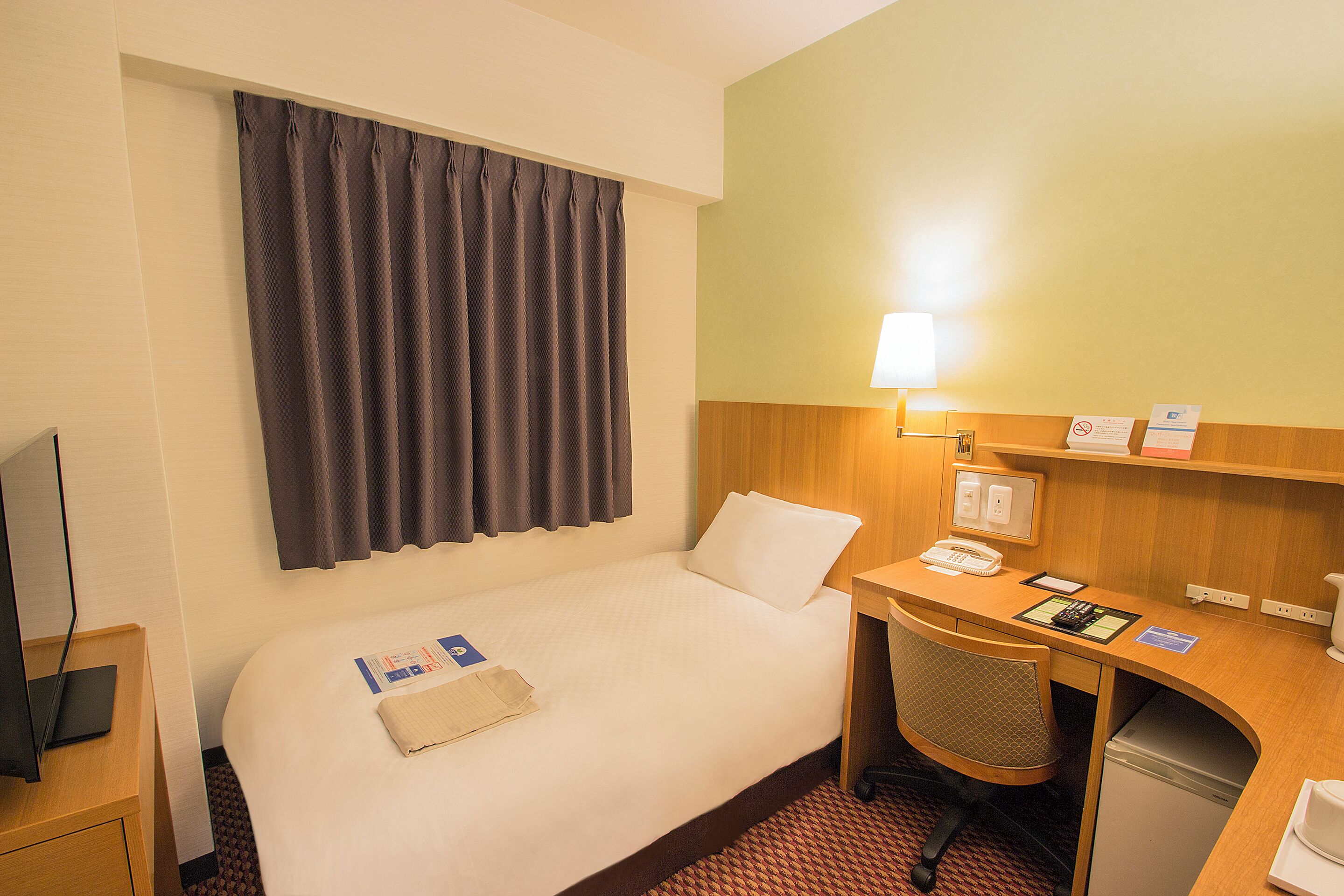 Una camera d'albergo con un letto, una scrivania, una sedia, una televisione e una lampada.