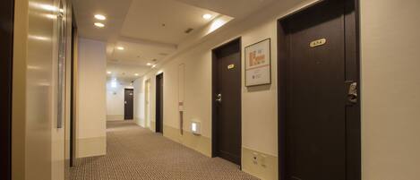 A hotel hallway with patterned carpet, dark doors, and recessed lighting.