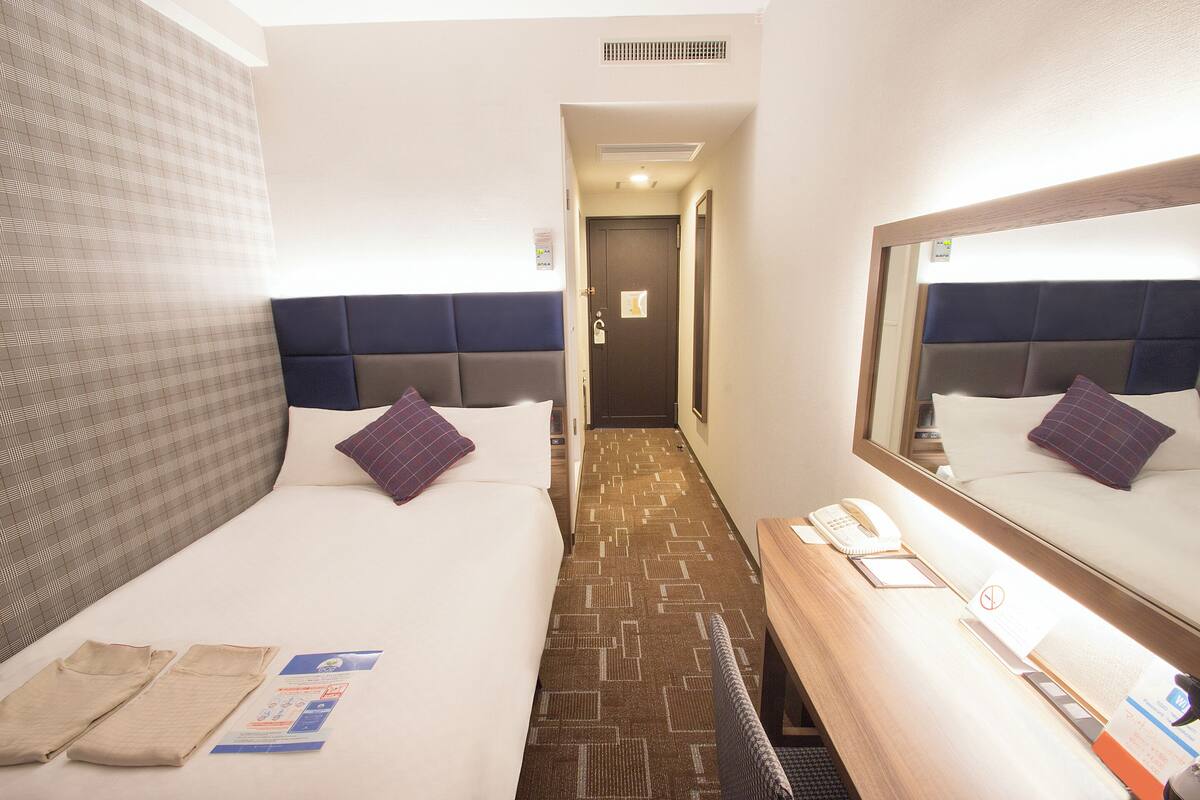 A hotel room with two beds, a desk with a telephone, and a mirror.