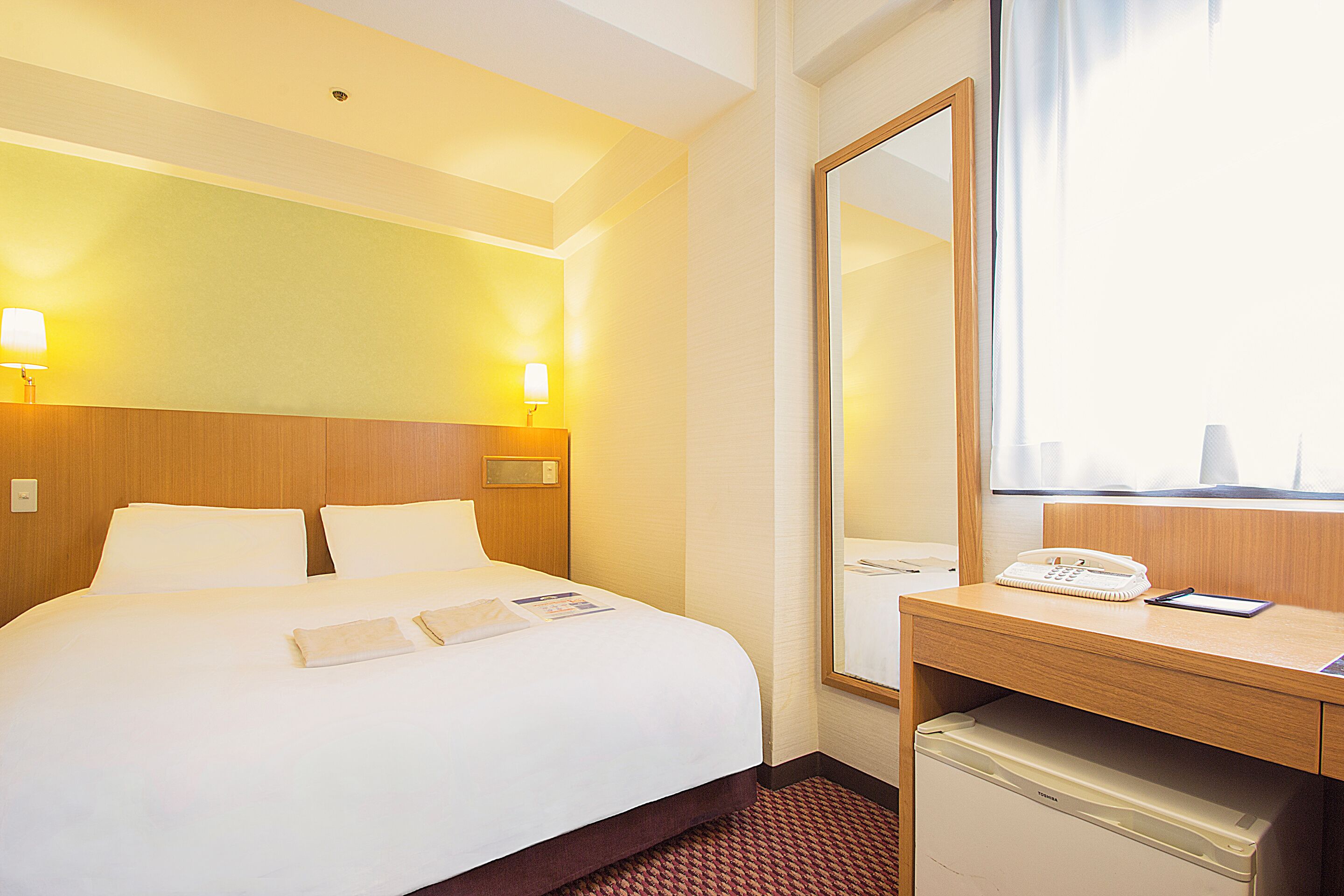 Une chambre d’hôtel comprenant un lit, des lampes de chevet, un bureau avec un téléphone et un miroir.