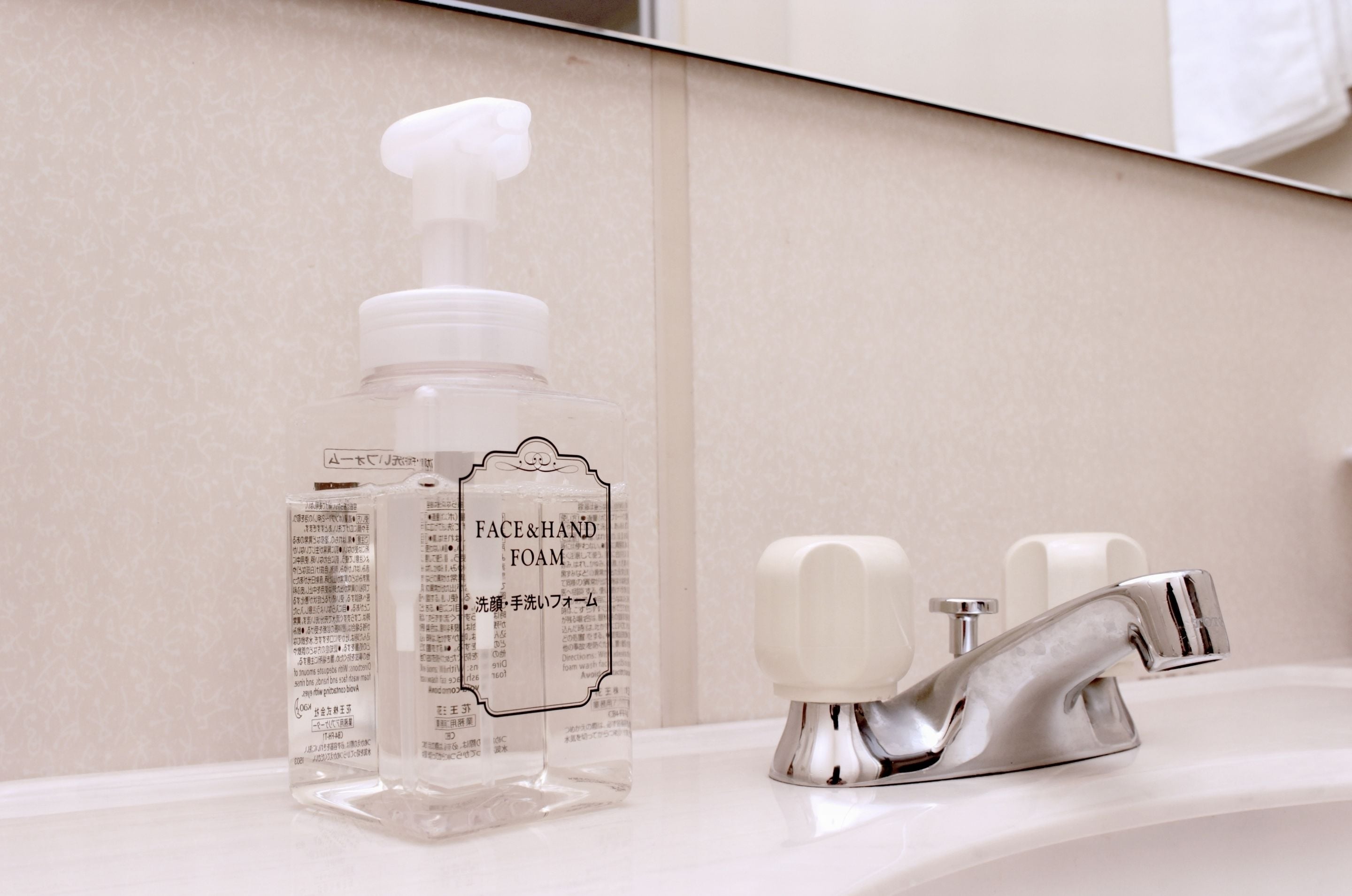 A bathroom with a clear bottle of face and hand foam, a chrome faucet, and a mirror.