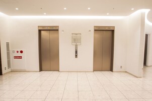 Un espace moderne pour les ascenseurs, comprenant deux ascenseurs, un panneau de commande d’alarme incendie et un sol dégagé.
