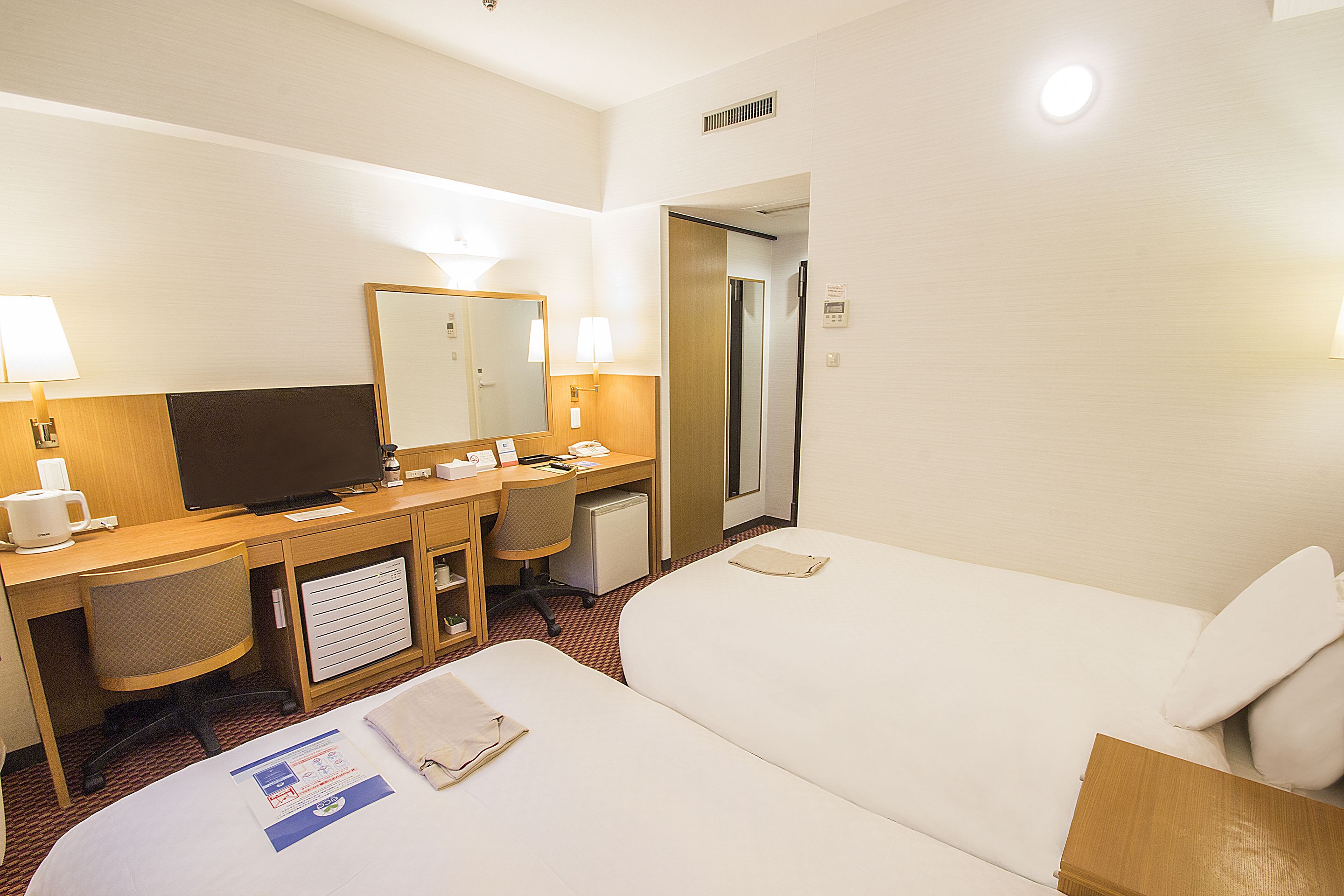 A hotel room with a bed, a desk with a computer, a chair, and a television.