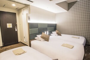 A hotel room with two beds, a dark door, a light switch, and a patterned wall.