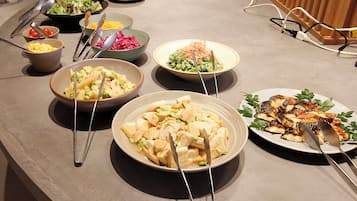 A buffet table with various dishes, including salads, vegetables, and meats, with serving utensils.