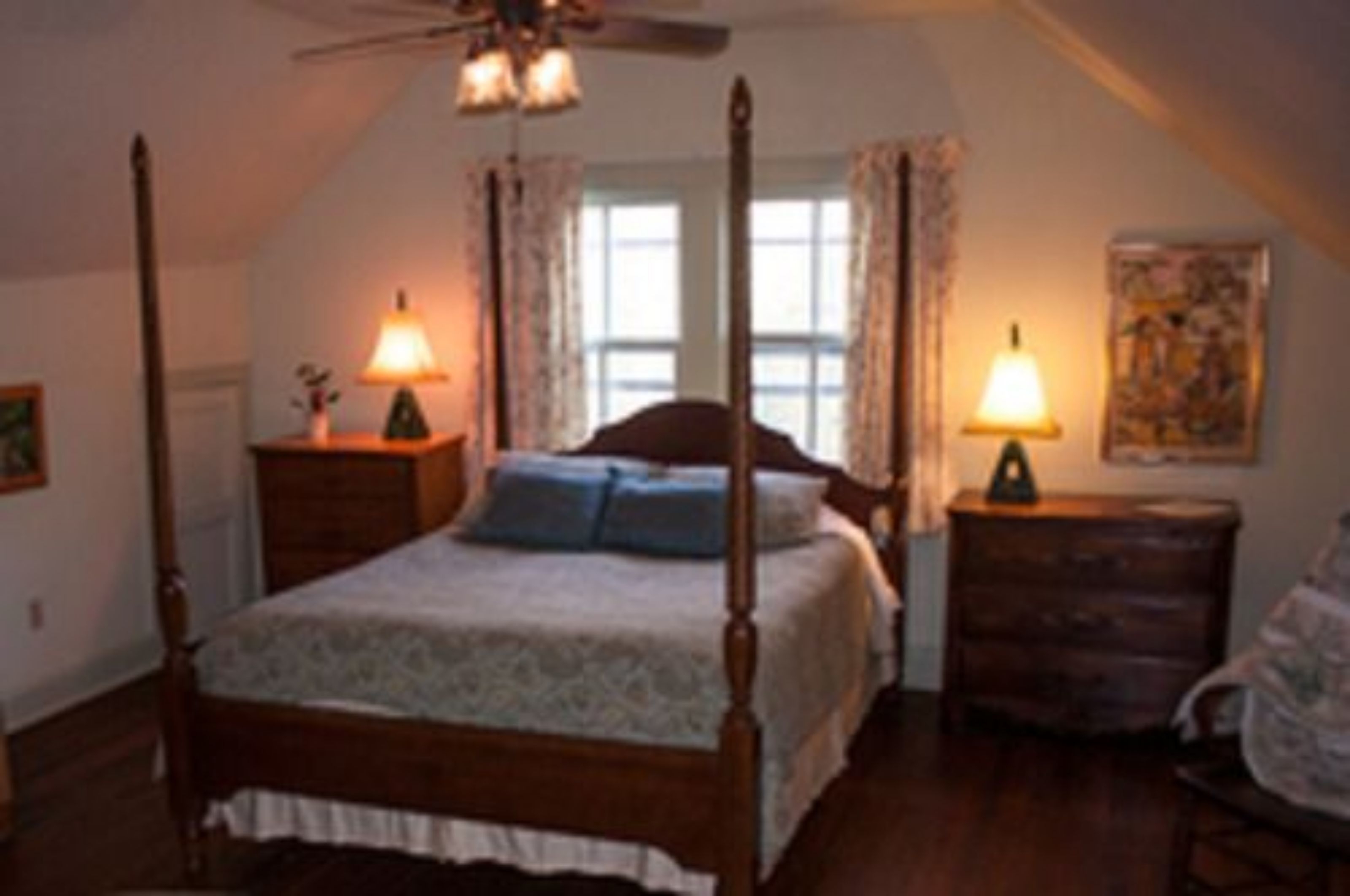 A four-poster bed with a wooden frame and a lace bedspread, flanked by two bedside tables with lamps.