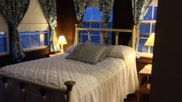 Un dormitorio con cama, cortinas, una ventana y una mesita de noche con lámpara.