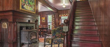 A grand staircase leading to a second floor, a wooden fireplace with a mantel, and a dining area with chairs and a table.
