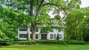 A two-story white house with a large tree in front, surrounded by lush greenery. - Black Mountain Inn (Black Mountain)