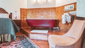 A vintage bathroom with a clawfoot bathtub, wooden paneling, a wooden chair, and a patterned rug. - Black Mountain Inn (Black Mountain)