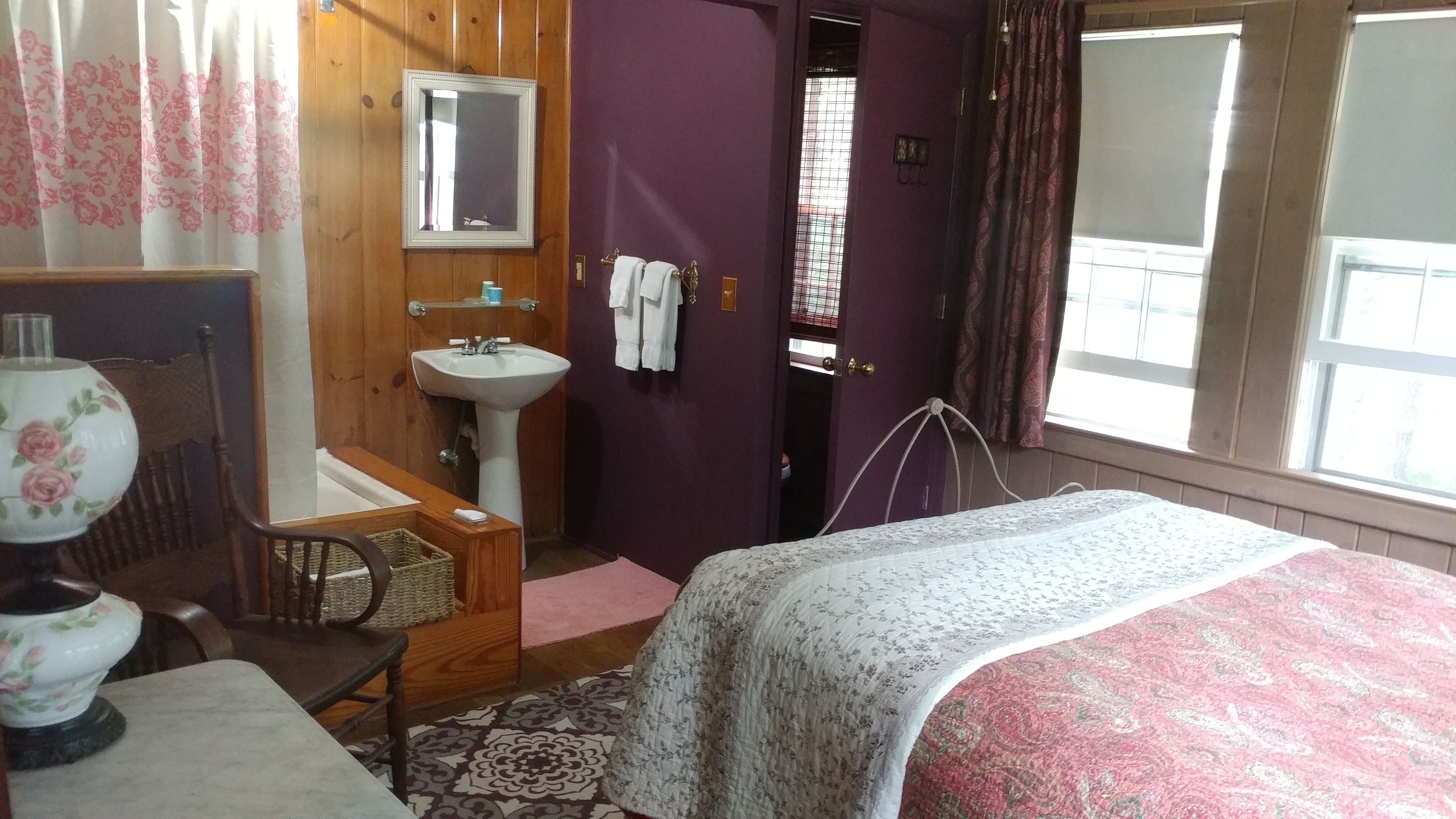 A bedroom with a bed, a bedside table, a lamp, a sink, and a mirror.