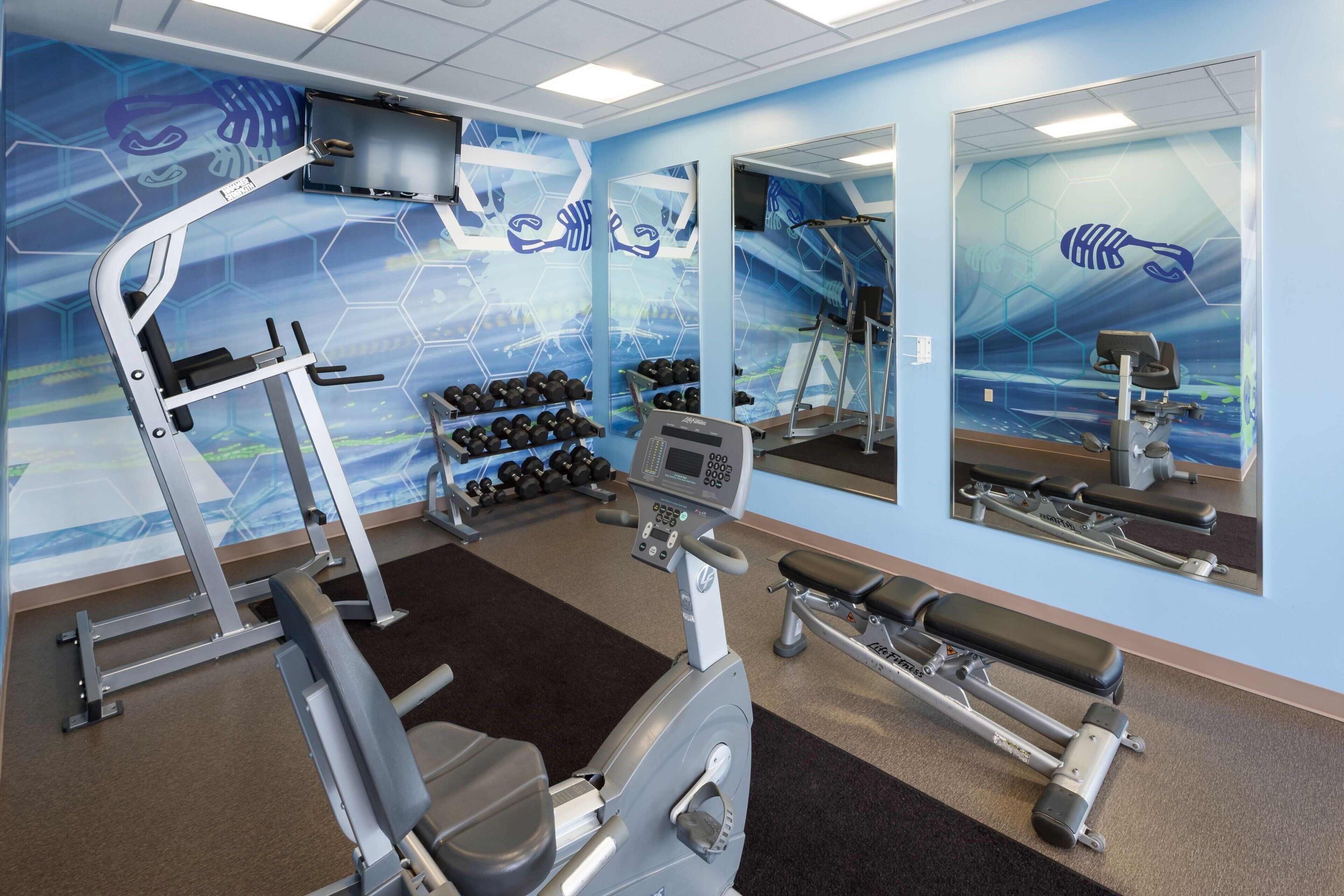 Un gimnasio con equipo de ejercicio, mancuernas y un espejo.