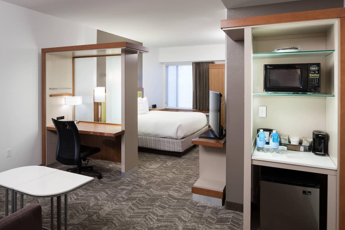 A hotel room with a bed, a desk with a chair, a television, a microwave, and a coffee maker.
