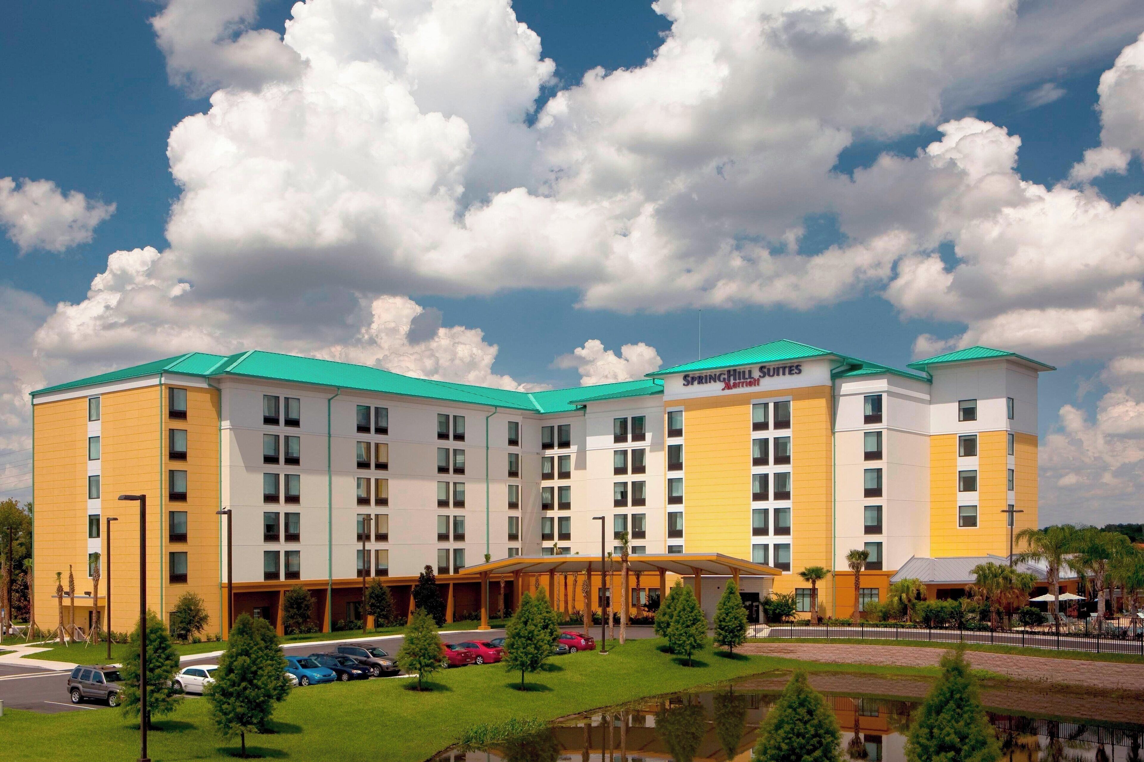 A multi-story hotel with a green roof, a swimming pool, and a parking lot.