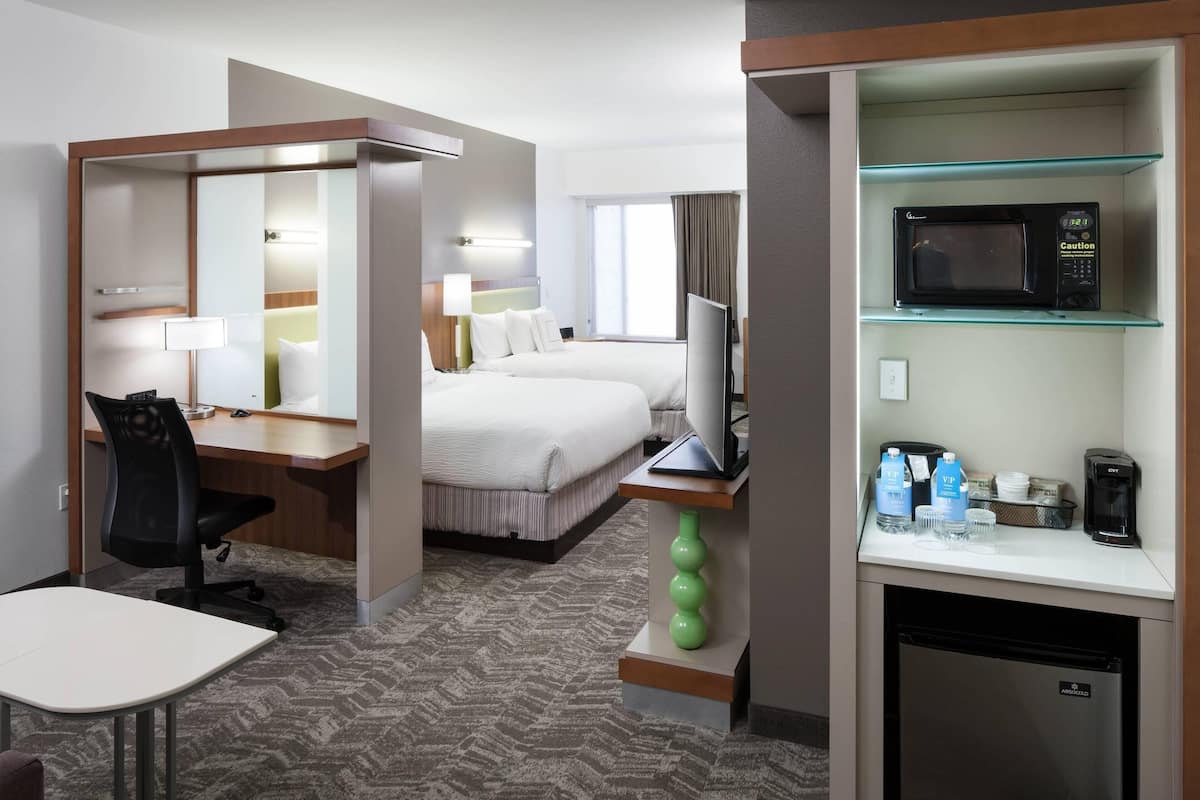 A hotel room with a bed, desk, chair, TV, microwave, and mini-fridge.