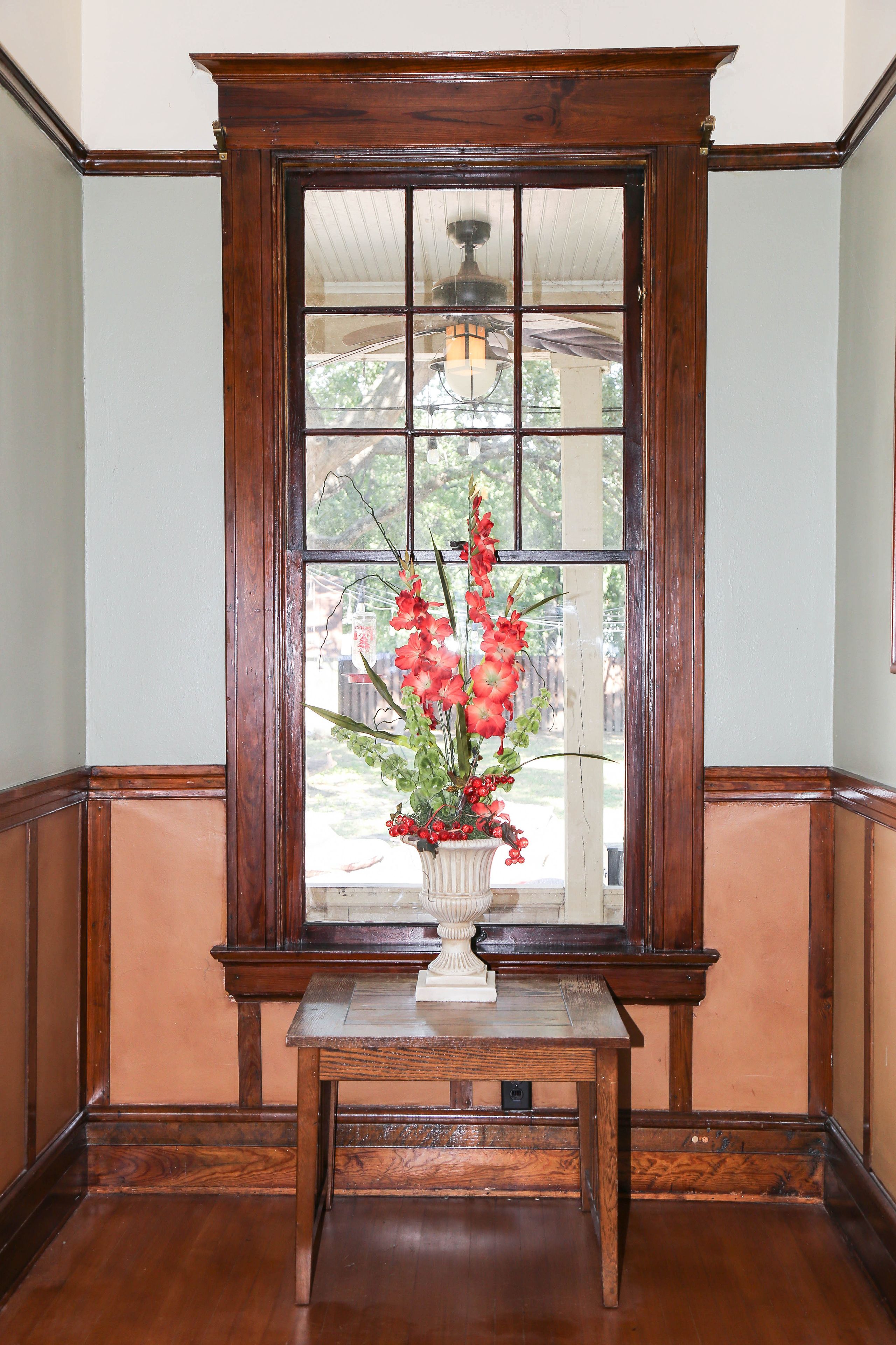 A wooden-framed window with a white vase containing red flowers.