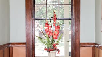 A wooden-framed window with a white vase containing red flowers.