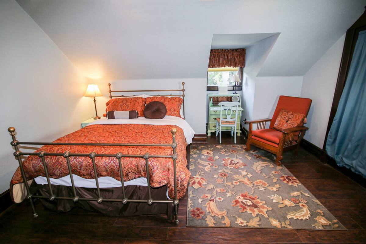 A bedroom with a bed, a chair, a desk, and a window.
