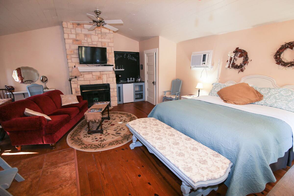 A cozy room with a fireplace, a bed with a blue bedspread, a red sofa, and a small table with a mirror.