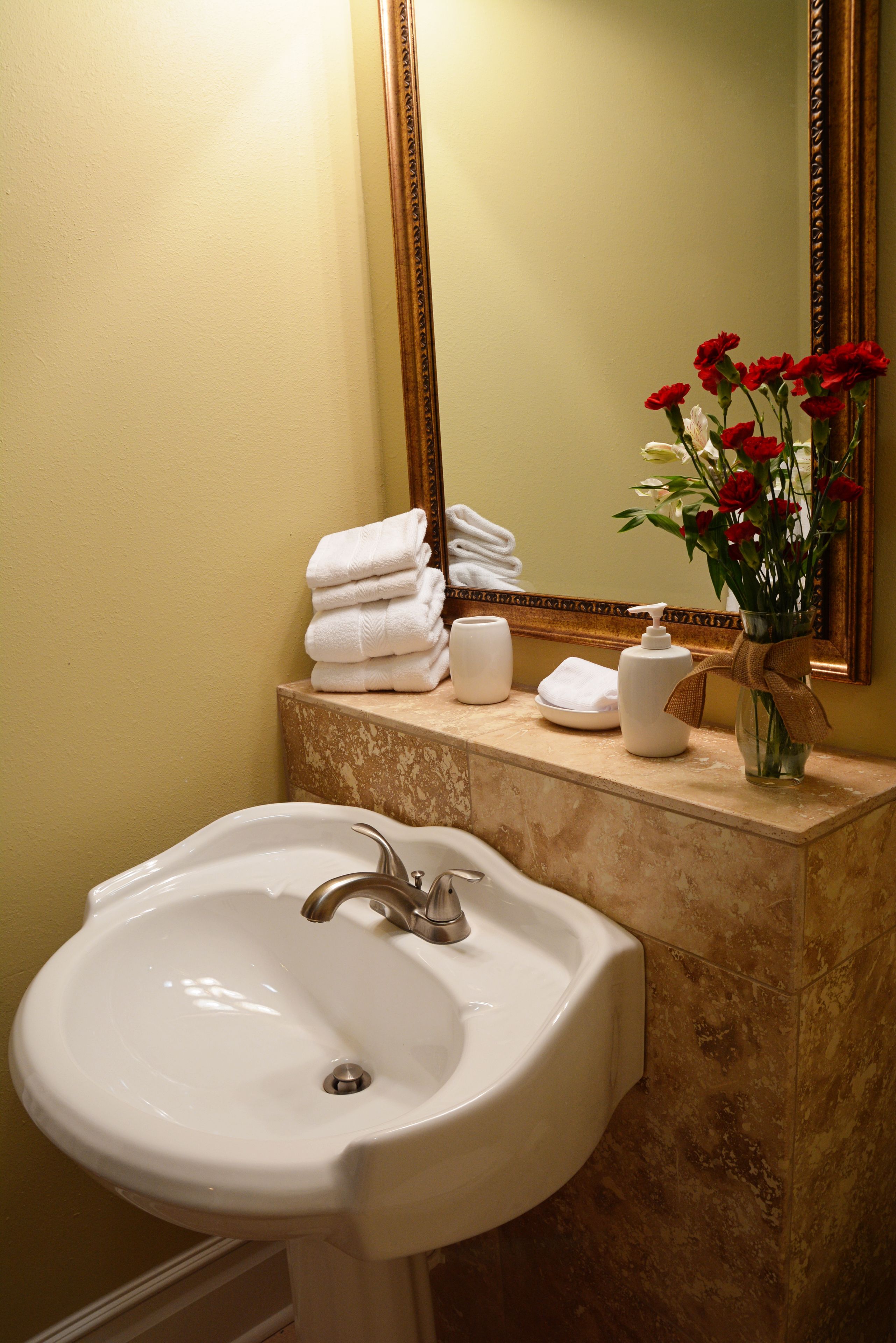 A bathroom with a sink, a mirror, and a vase with flowers.