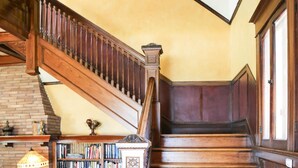 Un escalier en bois, agrémenté d’une bibliothèque et d’une lampe, se trouve dans une pièce aux murs jaunes et dotée d’une cheminée en briques.