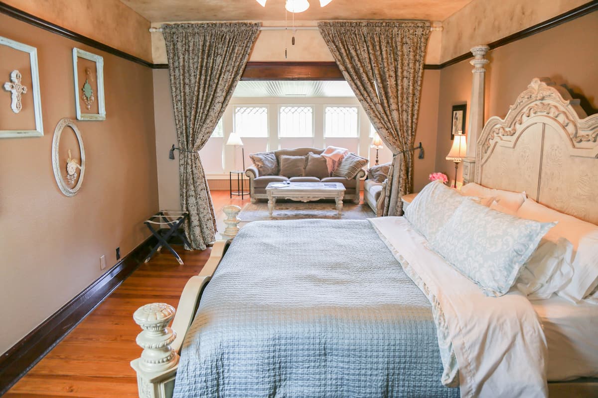 A bedroom with a large bed, a sofa, and a window with curtains.