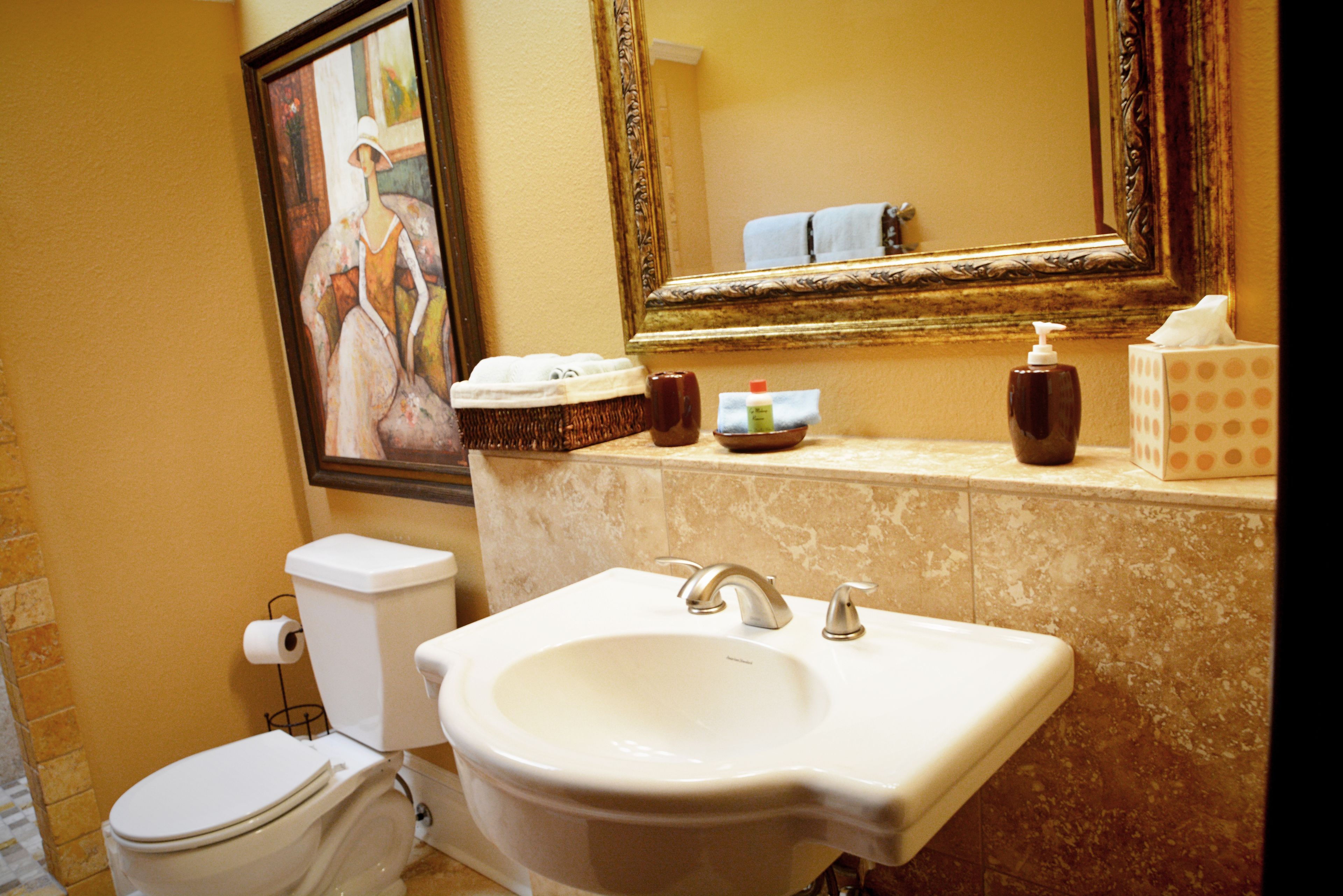 A bathroom with a toilet, sink, and a painting on the wall.