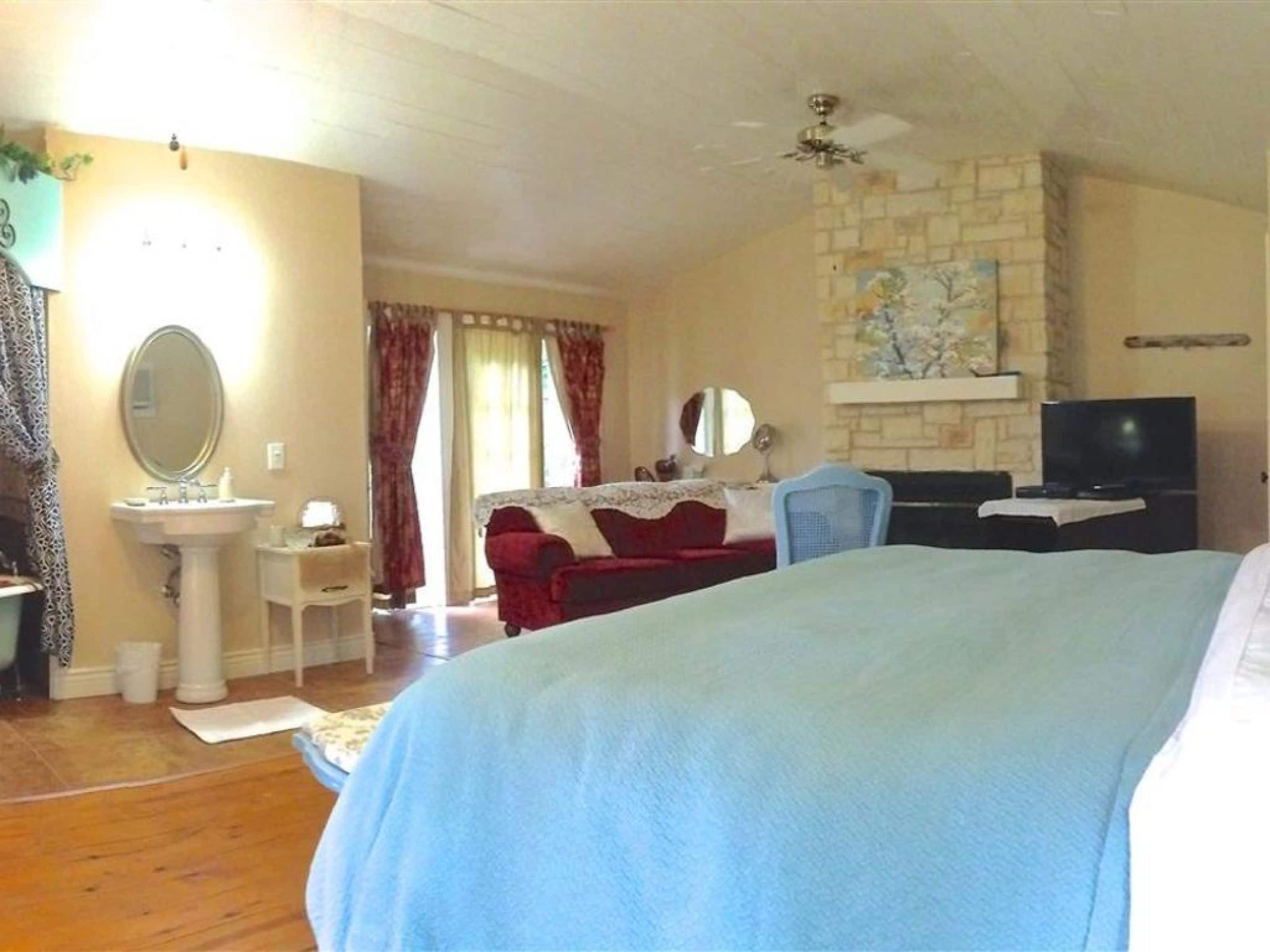 Ein Schlafzimmer mit Bett, Fernseher, kleinem Tisch, Stuhl, Spiegel und einem Badezimmer mit Waschbecken und Toilette.