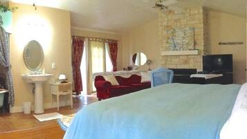 Ein Schlafzimmer mit Bett, Fernseher, kleinem Tisch, Stuhl, Spiegel und einem Badezimmer mit Waschbecken und Toilette.
