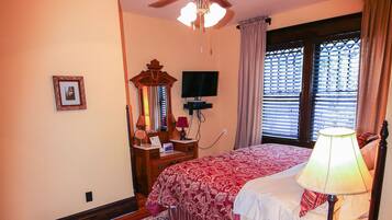 A bedroom with a bed, a ceiling fan, a nightstand, a lamp, a mirror, a dresser, a TV, and a window with curtains.