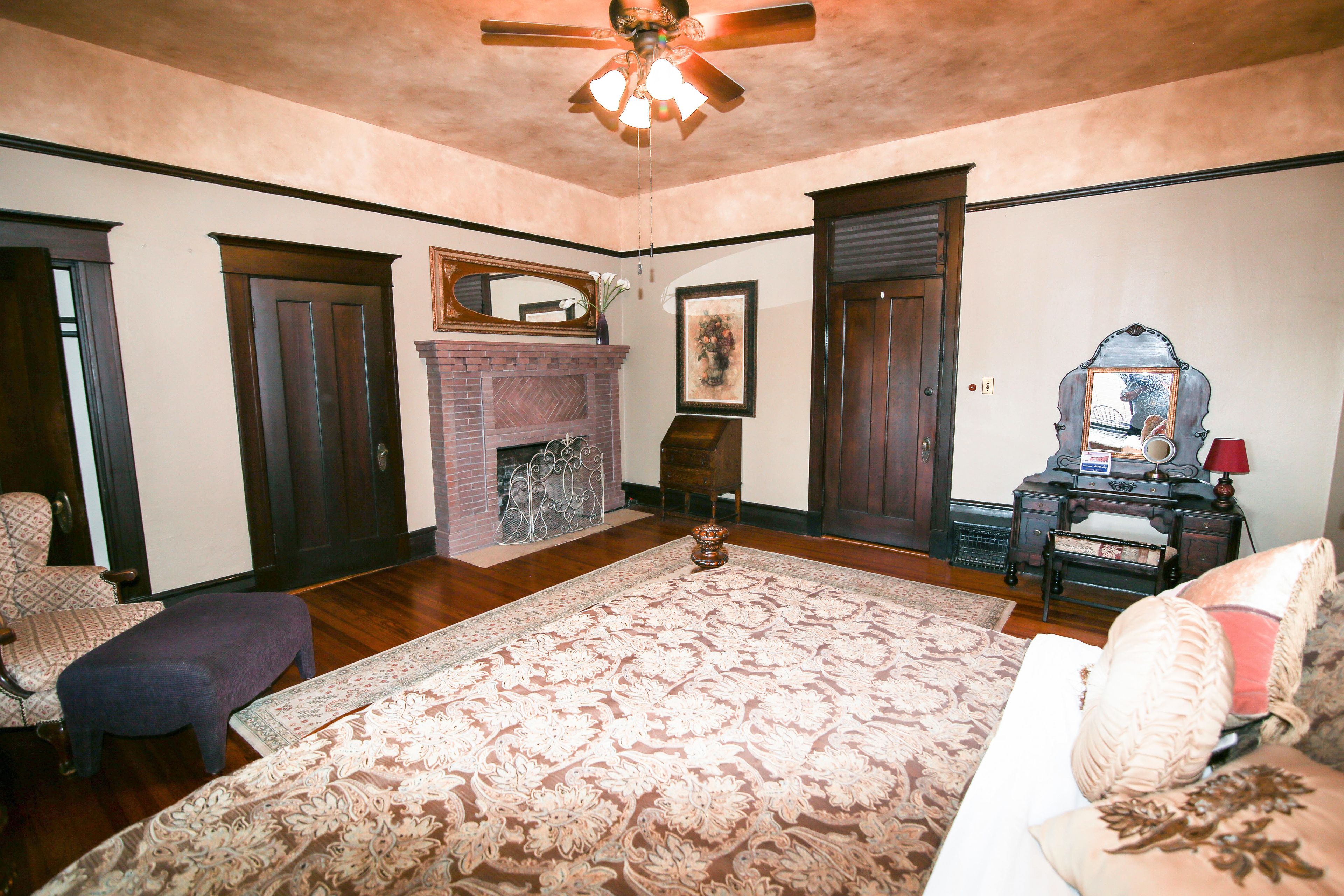 Una habitación amplia con pisos de madera, un tapete grande con estampado floral, una chimenea y un escritorio antiguo con un espejo.