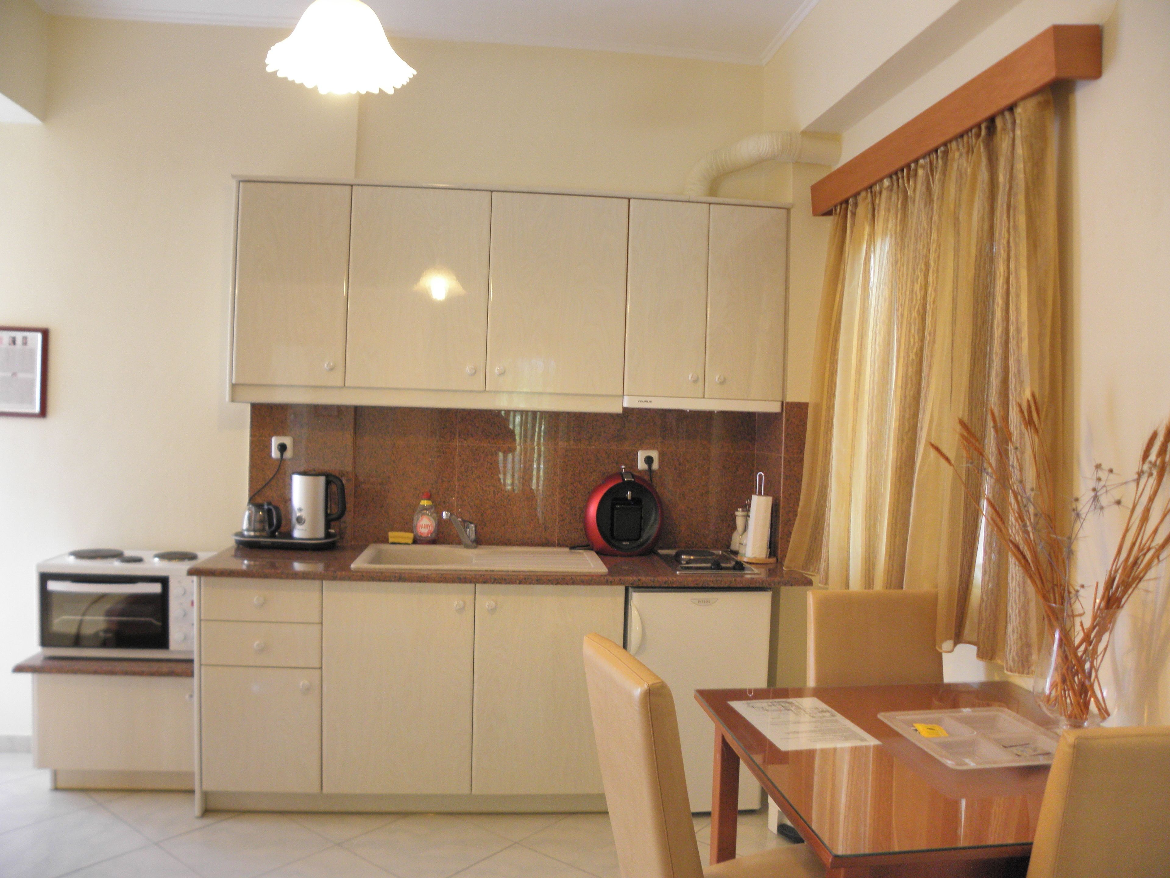 A compact kitchen with a microwave, kettle, and coffee maker. There is a dining table with chairs and a vase with dried plants.